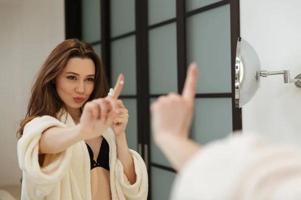 Женщина со сливками на пальце смотрит на зеркало в ванной комнате — стоковое фото