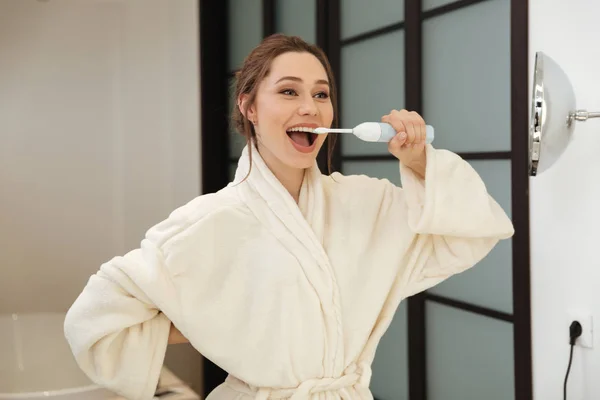 Ευτυχισμένη γυναίκα στέκεται και να βουρτσίζετε τα δόντια της στο μπάνιο — Φωτογραφία Αρχείου