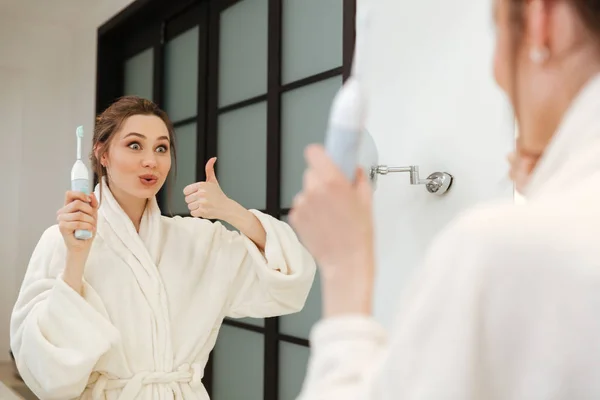 Ευτυχισμένη γυναίκα βούρτσισμα των δοντιών και δείχνει τους αντίχειρες επάνω στο μπάνιο — Φωτογραφία Αρχείου