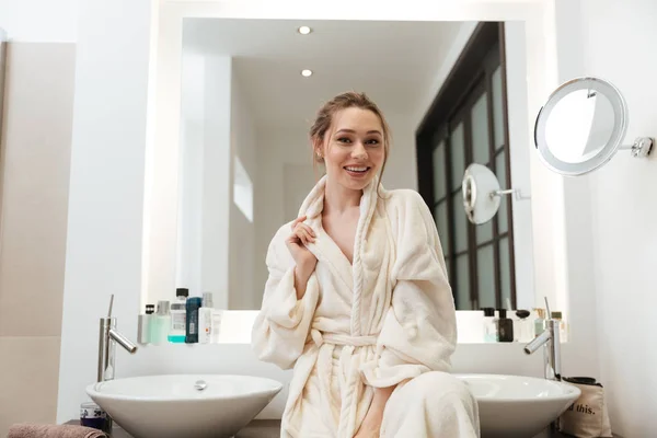 バスルームにバスローブで陽気な美しい若い女性 — ストック写真