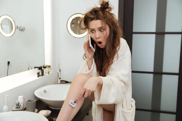Erstaunte geschockte Frau rasiert Beine und telefoniert — Stockfoto