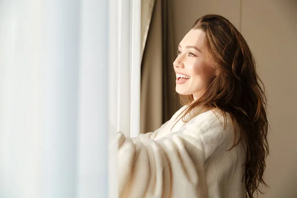 Mulher alegre em roupão de banho sorrindo e olhando para a janela — Fotografia de Stock