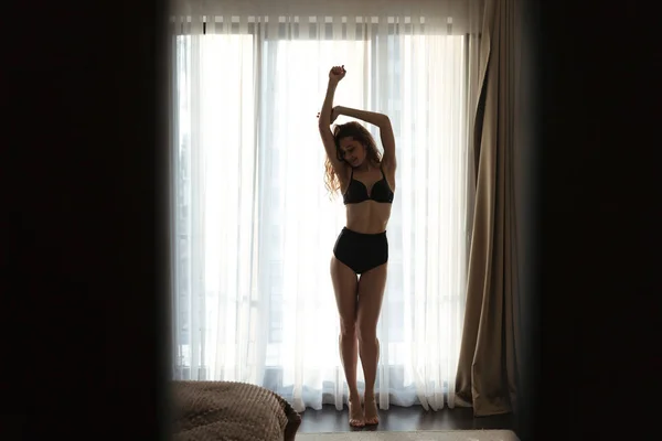 Silhouette di attraente giovane donna in lingerie in piedi vicino alla finestra — Foto Stock