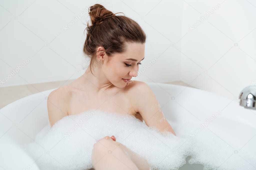 Smiling beautiful young woman sitting in bath with foam