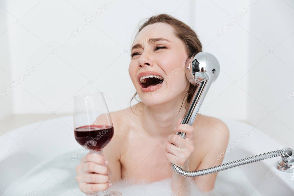 Sad woman with glass of wine crying in bathtub