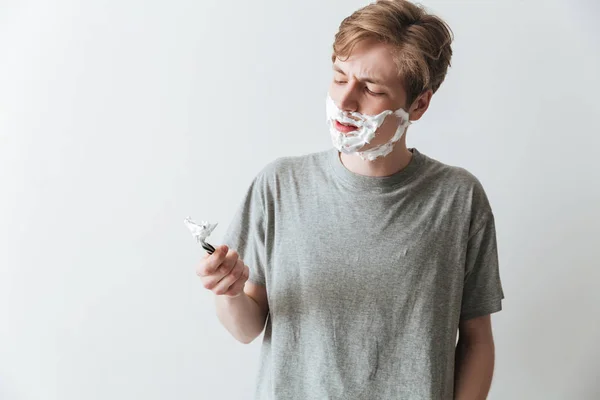 Displeased man in  shaving foam holding razor — Stock Photo, Image