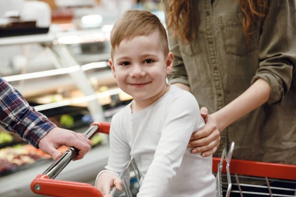 Happy young boy sitting in shopping trolley and looking camera — Stock Photo, Image