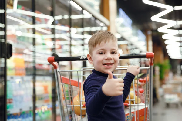 Niño feliz cerca de carrito de compras mostrando el pulgar hacia arriba — Foto de Stock