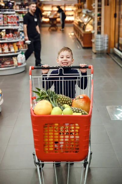 Imagem vertical de menino feliz empurrando carrinho de compras — Fotografia de Stock