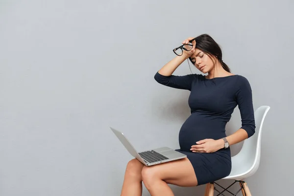 Mujer embarazada cansada sentada sobre fondo gris —  Fotos de Stock