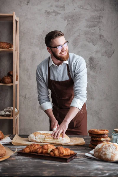 Glücklicher junger Mann Bäcker steht beim Bäcker und schneidet das Brot. — Stockfoto