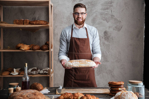 Cheerful young man baker standing at bakery holding bread