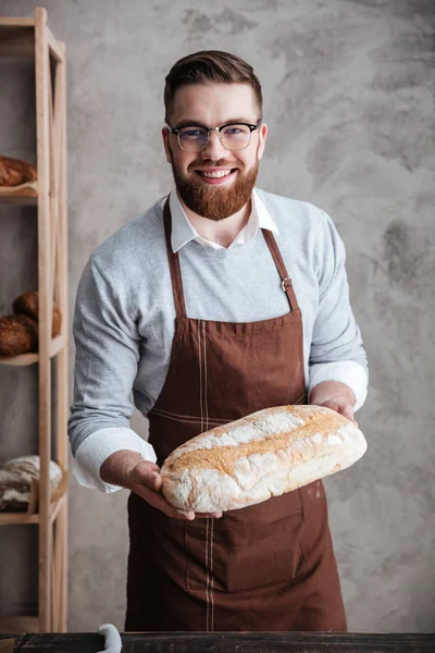 Glad ung man baker står vid bageriet håller bröd — Stockfoto