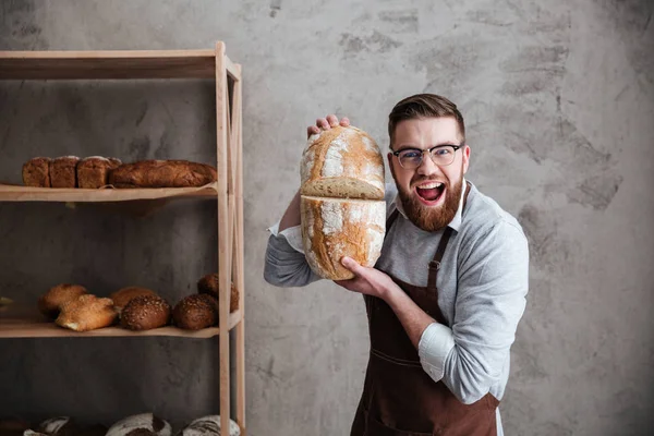 Skrikande unge mannen baker står vid bageriet håller bröd — Stockfoto