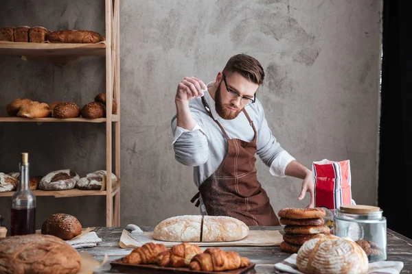 Homem concentrado padeiro em pé na padaria perto de pão — Fotografia de Stock