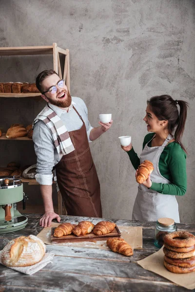 Cheerful loving couple bakers drinking coffee. Looking aside. — Stock Photo, Image