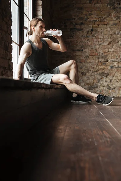 Retrato de um desportista cansado bebendo água de uma garrafa — Fotografia de Stock