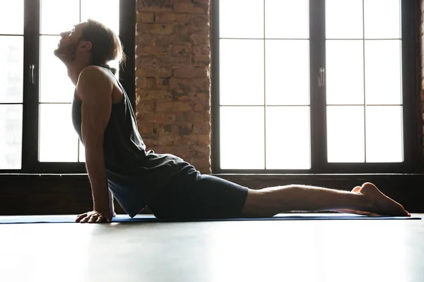 Молодой концентрированный спортсмен растягивает мышцы на коврике для фитнеса — стоковое фото