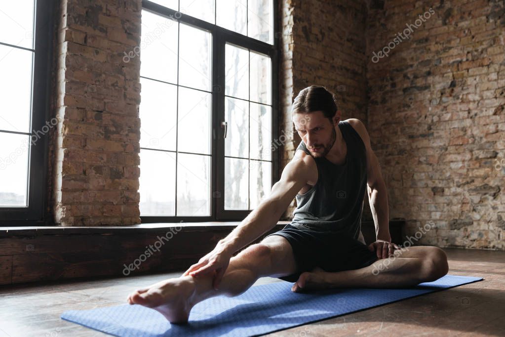 Young concentrated sportsman stretching muscles on the fitness mat
