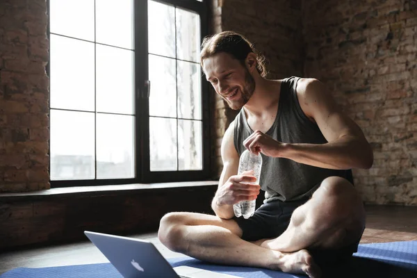 Happy strong sportsman drinking water on floor in gym — Stock Photo, Image
