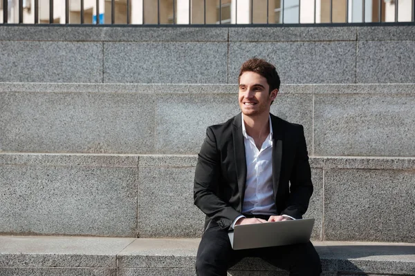 Feliz joven hombre de negocios sentado al aire libre utilizando el ordenador portátil — Foto de Stock