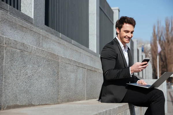 Souriant jeune homme d'affaires assis à l'extérieur bavarder par téléphone . — Photo