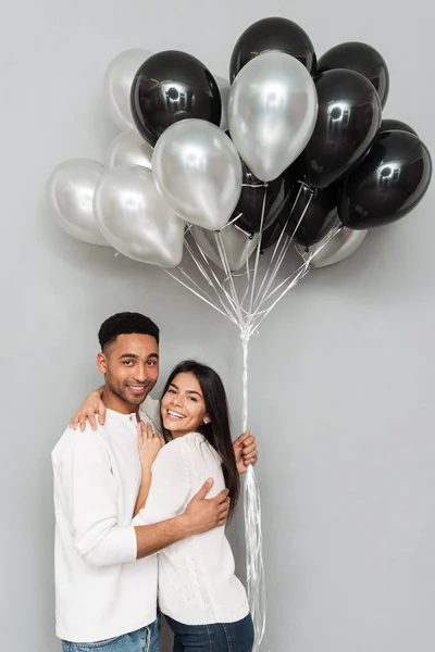 Veselá milující pár stojící nad šedou zeď s balónky. — Stock fotografie