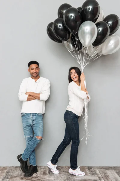 Šťastné milující pár stojící nad šedou zeď s balónky — Stock fotografie