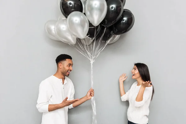 Glückliches Liebespaar steht mit Luftballons über graue Wand — Stockfoto