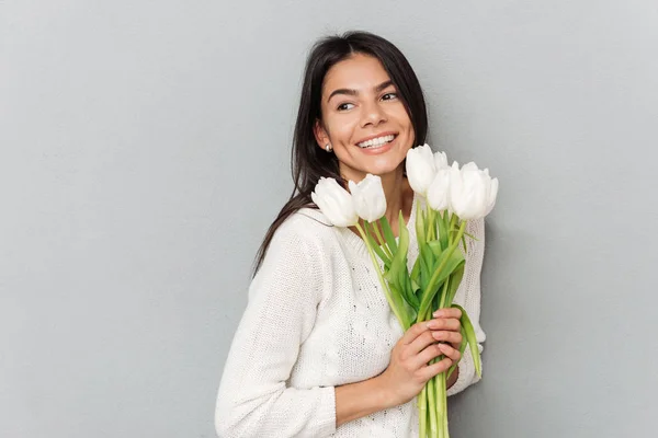 Mulher alegre em pé sobre a parede cinza com flores — Fotografia de Stock