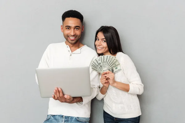 Hombre joven usando portátil cerca de su mujer con dinero —  Fotos de Stock