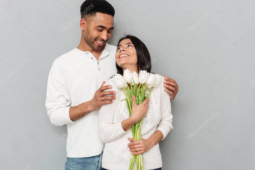 Smiling loving couple standing over grey wall with flowers