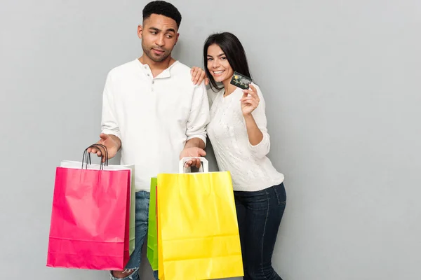 Casal amoroso em pé sobre a parede cinza e segurando sacos de compras — Fotografia de Stock