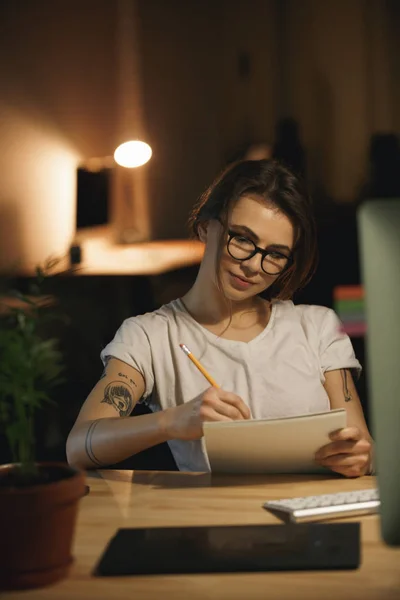 Ernsthafte junge Designerin, die nachts drinnen sitzt und Notizen schreibt — Stockfoto