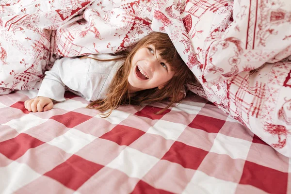 Счастливый ребенок на кровати под одеялом — стоковое фото