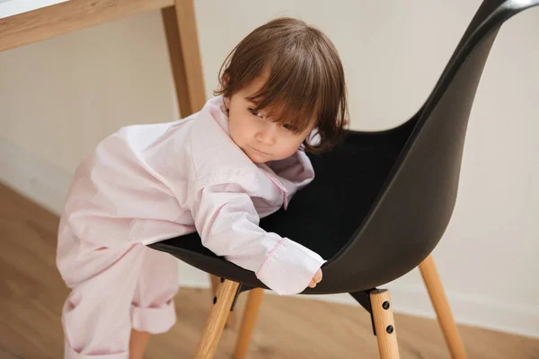 Милая маленькая девочка в пижаме забирается на стул — стоковое фото