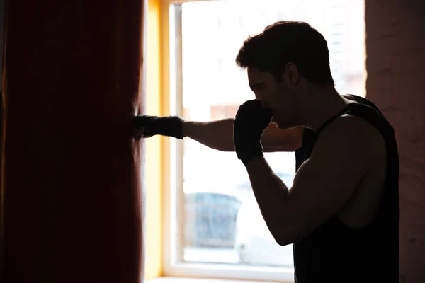 Человек в тени пинает боксерскую грушу — стоковое фото