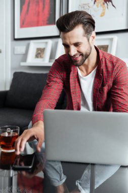 Mutlu genç telefon tutarak dizüstü bilgisayar kullanan adam sakallı