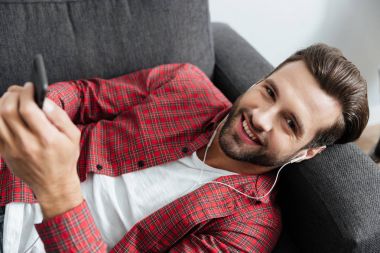 Neşeli genç adam kanepede kapalı telefonla sohbet yatıyor.