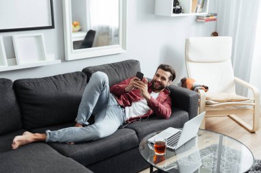 Neşeli genç adam kanepe telefonla sohbet üzerinde yatıyor.