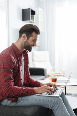 Kapalı dizüstü bilgisayar kullanarak koltukta oturan gülümseyen genç adam