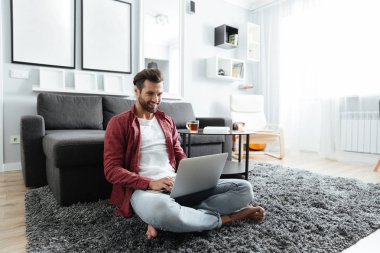 Kapalı dizüstü bilgisayar kullanırken evde oturan genç adam gülümseyen