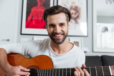 Mutlu bir adam gitar çalmaya. Kameraya bakarak.