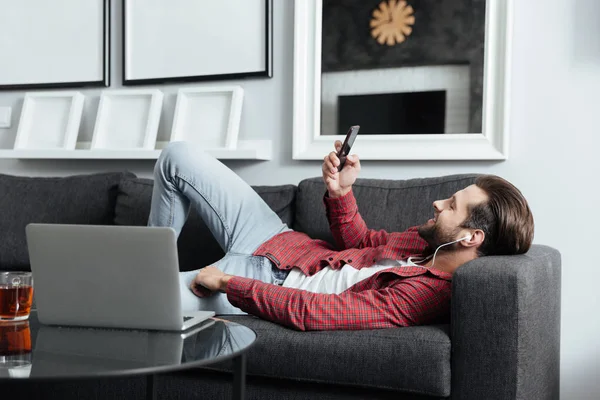 Счастливый молодой человек лежит на диване, слушает музыку с наушниками — стоковое фото