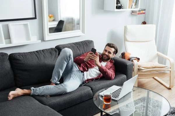 Joyeux jeune homme se trouve sur le canapé bavarder par téléphone . — Photo