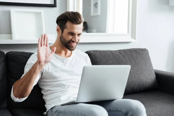 Lächelnder junger Mann sitzt zu Hause und benutzt Laptop — Stockfoto