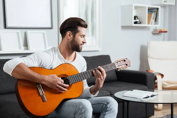 Sonriente hombre sentado en el sofá tocando la guitarra — Foto de Stock
