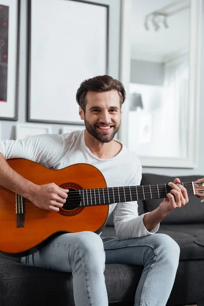 Lycklig man sitter på soffa spela på gitarr. — Stockfoto