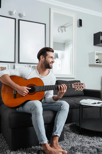 Щасливий чоловік сидить на дивані, граючи на гітарі . — стокове фото