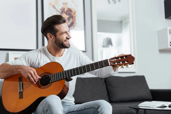 Hombre feliz sentado en el sofá tocando la guitarra — Foto de Stock
